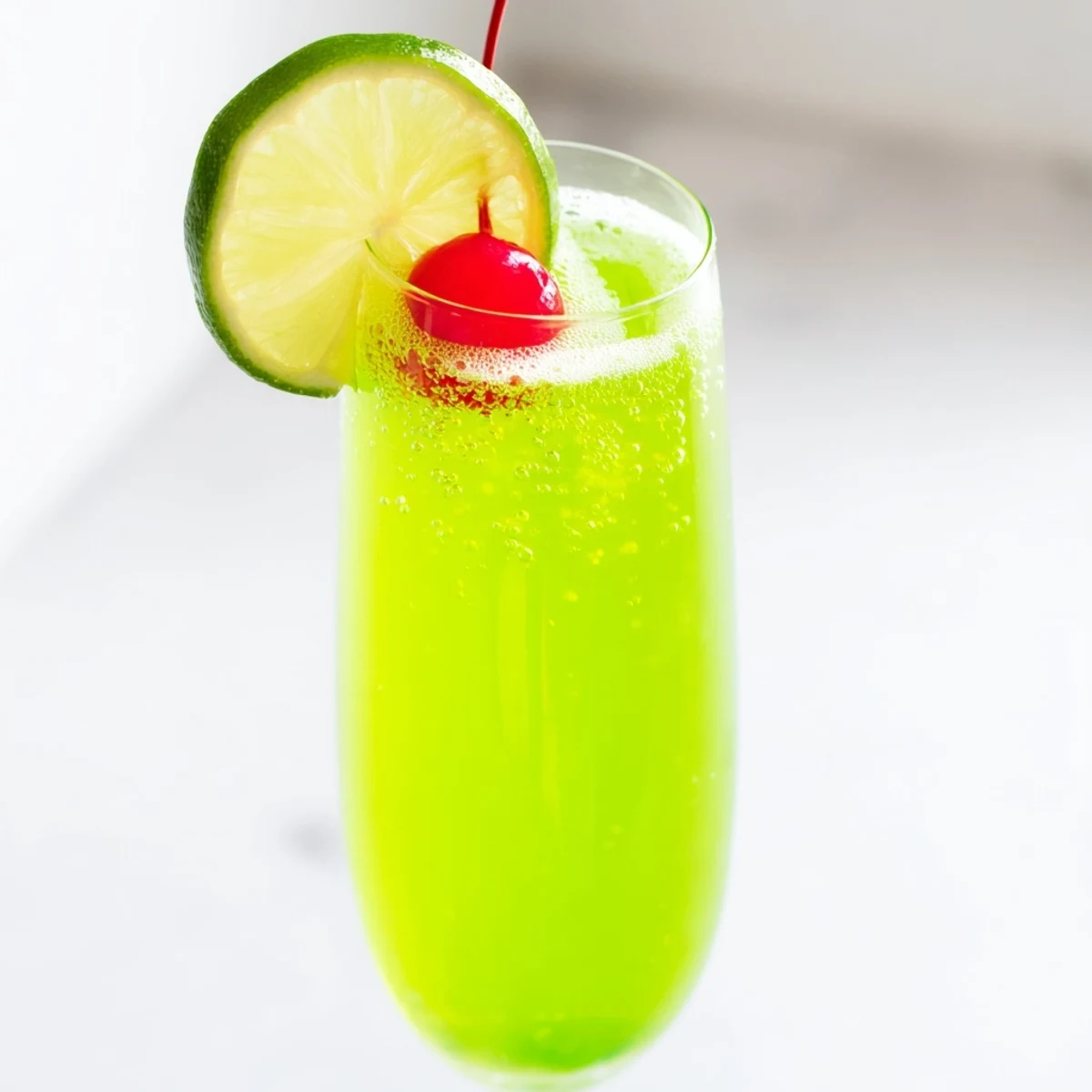 Bright green Quick Grinch Mimosa Mocktail boasts maraschino cherries and lime, ready for festive sipping.