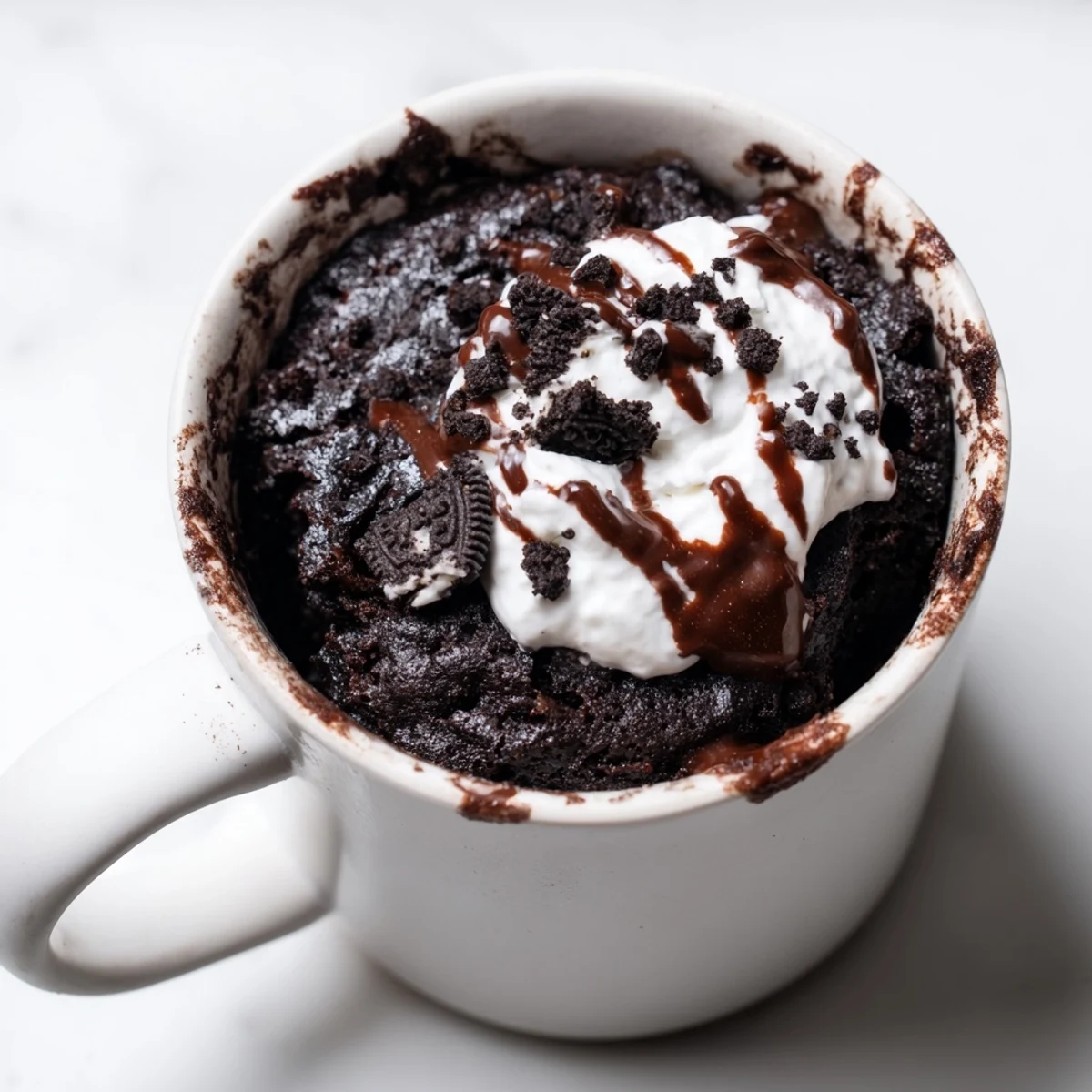 Fudgy Oreo mug cake, a quick chocolate dessert, sits ready to eat with whipped cream.