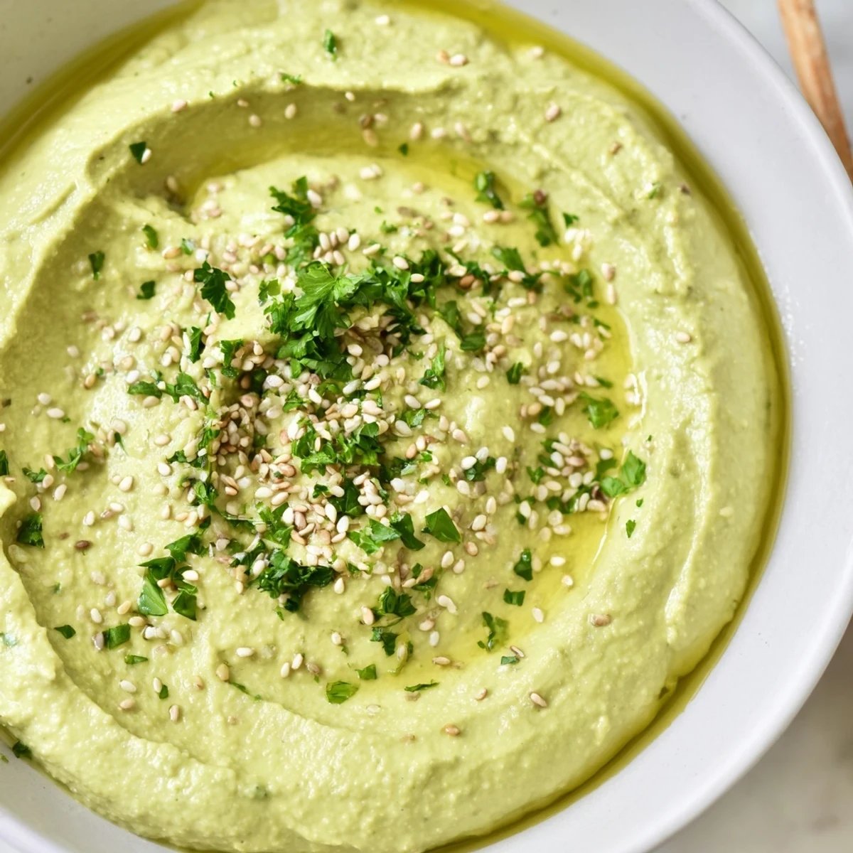 Creamy edamame hummus swirled with olive oil, ready to scoop with fresh vegetables for dipping.
