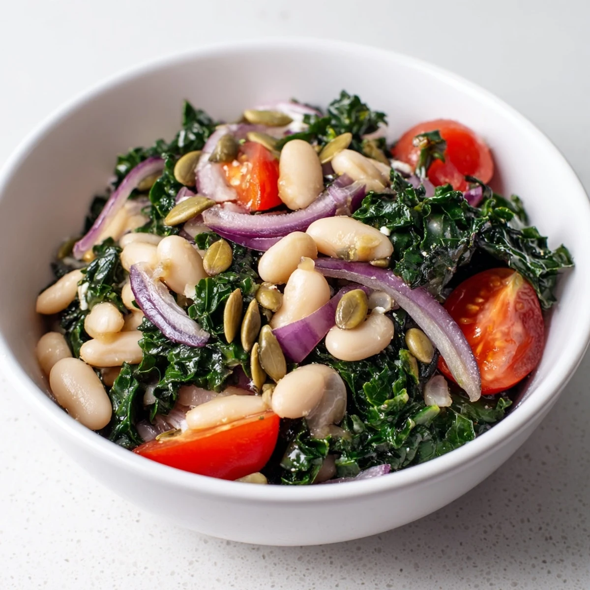 A vibrant bowl of White Bean and Kale Salad features creamy beans, massaged kale, and bright lemon-garlic dressing, topped with toasted seeds and cherry tomatoes.  