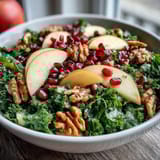 Two beautiful servings of a Kale and Pomegranate Bowl featuring tender greens, crisp apple slices, ruby-red seeds, and chopped walnuts ready for a healthy lunch or side dish.