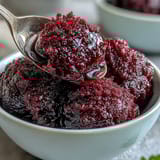 A vibrant scoop of Black Currant Sorbet served in a chilled glass dish, showing its deep purple hue and smooth texture.