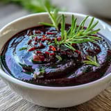 A small glass jar holds the deep purple Black Currant and Rosemary Reduction, with a spoon dipping into the thick sauce.