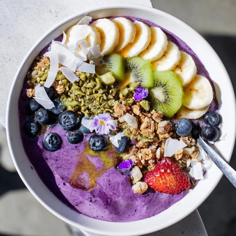 Vibrant smoothie bowls with pistachio and purple yam, topped with fresh fruit.  