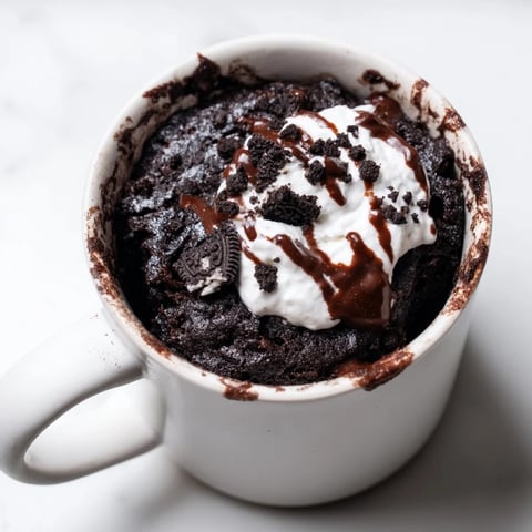Fudgy Oreo mug cake, a quick chocolate dessert, sits ready to eat with whipped cream.