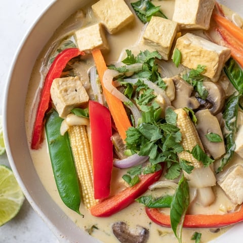 Steaming bowl of Thai Green Curry Coconut Soup, garnished with vibrant cilantro and lime wedges.