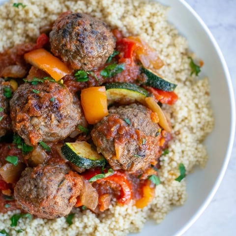 Golden kefta meatballs simmer in a spiced tomato sauce, served over fluffy couscous for a taste of North Africa.