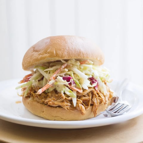 Tender pulled barbecue chicken piled high on a soft, toasted brioche bun, crowned with a vibrant, tangy cabbage slaw for a satisfying bite.