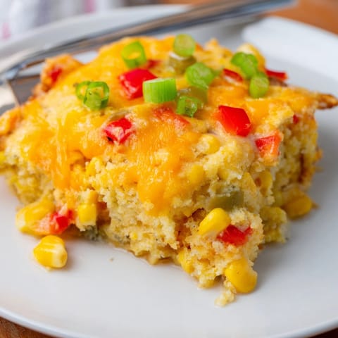 Slices of warm Cheesy Cajun Cornbread Casserole, showing moist crumbs and colorful veggies.