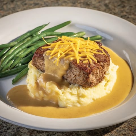 A delicious close-up of a plated Pork Chops & Cheddar Mash Bowl with savory pan gravy and vibrant green beans.