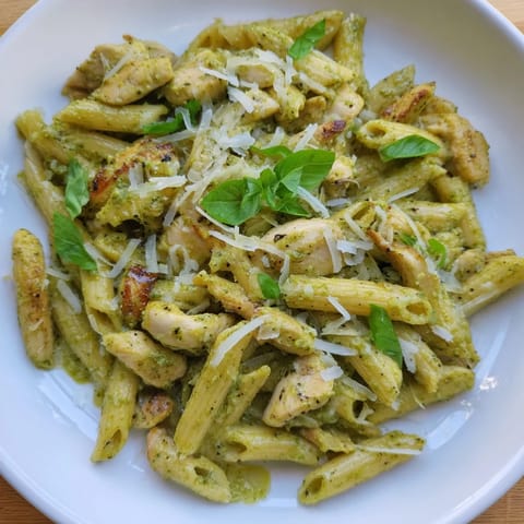 A close-up of Creamy Pesto Penne & Chicken ready to serve, garnished with fresh basil leaves.