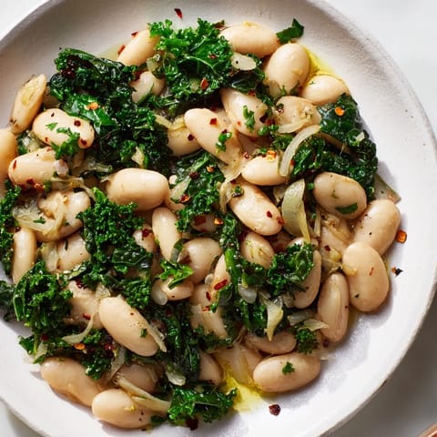A close-up of steaming garlicky beans with vibrant winter greens, ready for serving this side.