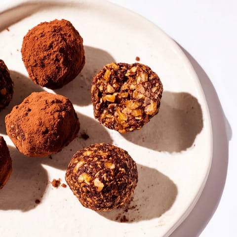 Close-up of freshly made Date & Walnut Truffles with a light cocoa dusting, ready to savor.
