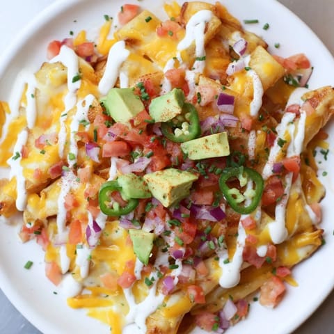 A close-up of cheesy Pasta Chips Nachos with vibrant red tomatoes and green cilantro.