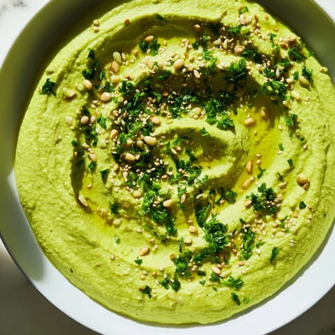 A close-up of vibrant green edamame hummus garnished with sesame seeds and parsley.