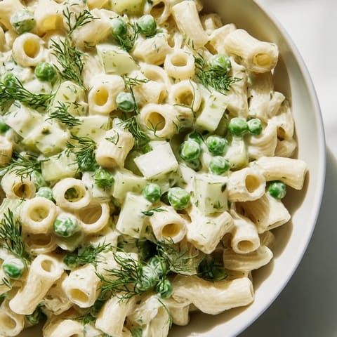 Creamy Dill Pickle Pasta Salad in a white bowl with a wooden spoon, featuring ditalini pasta mixed with green peas and diced pickles.  
