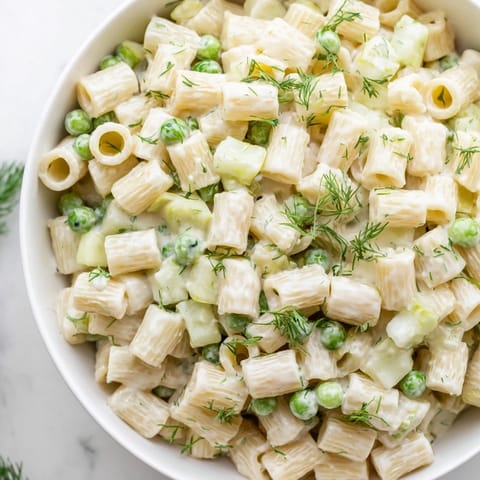 A chilled bowl of Creamy Dill Pickle Pasta Salad garnished with fresh dill, ready for a summer picnic or backyard barbecue.  