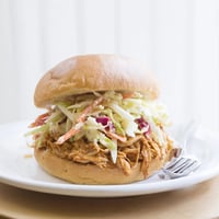 Tender pulled barbecue chicken piled high on a soft, toasted brioche bun, crowned with a vibrant, tangy cabbage slaw for a satisfying bite.