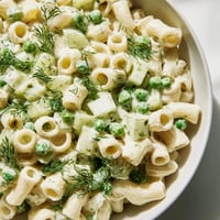 Creamy Dill Pickle Pasta Salad in a white bowl with a wooden spoon, featuring ditalini pasta mixed with green peas and diced pickles.  